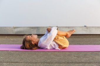 Kinder Yoga. Kind liegt auf einer Yogamatte mit angezogenen Beinen auf dem Rücken und entspannt.